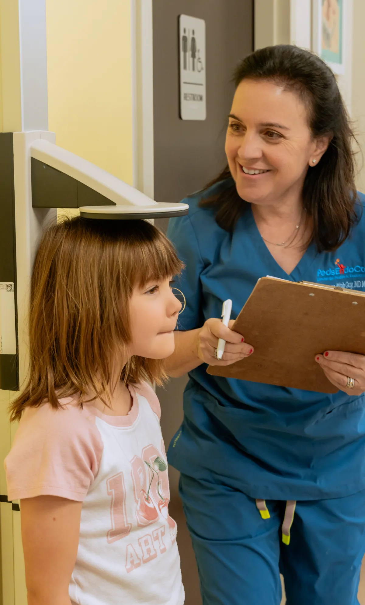 Dr. Aftab Guy measuring a young patient's height against the growth chart