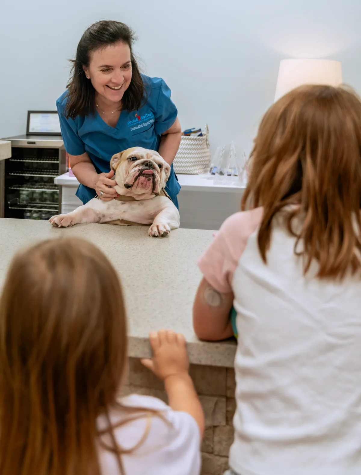 Dr. Aftab Guy with Georgy the therapy dog on the exam table and two young patients